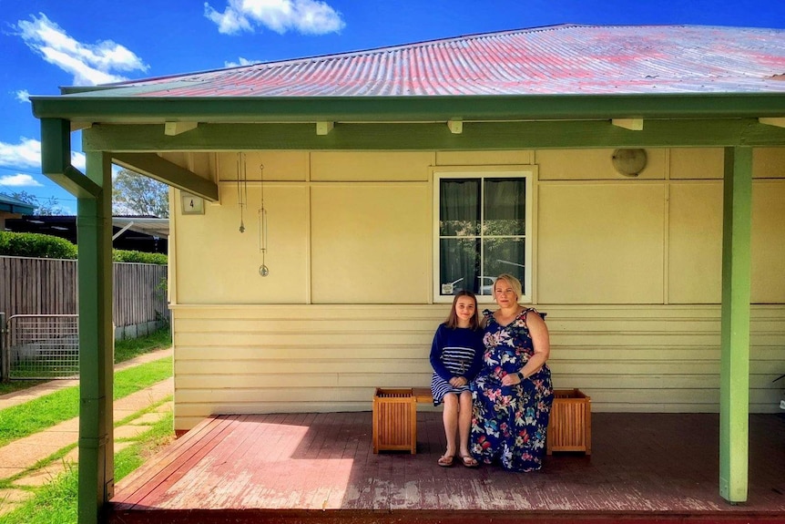 Natalie and Celeste sit on their verandah and smile.