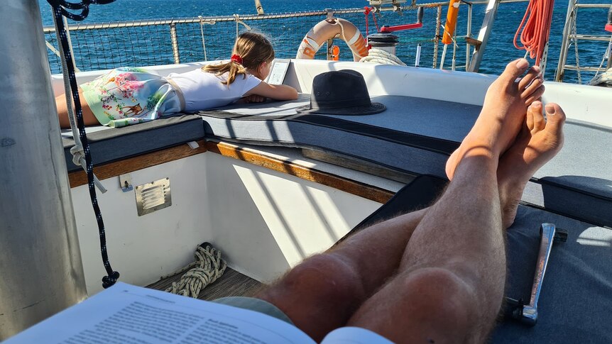 A father and child relax onboard a sailing boat. 