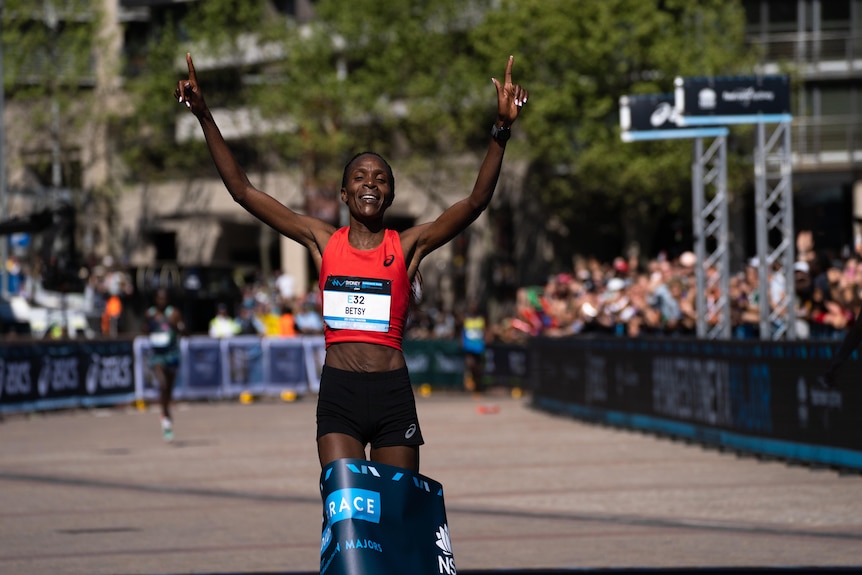 woman holds up hands in joy while crossing finishing ribbon