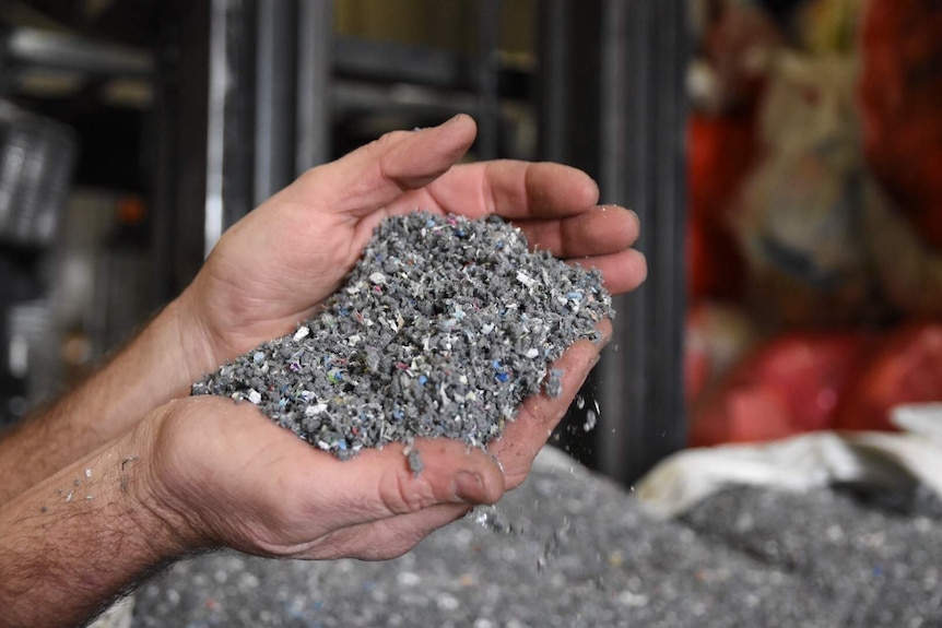 A man holds grey crushed up recycled plastics in his both of his hands.