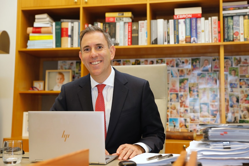 Jim Chalmers smiles behind a desk with a laptop. 