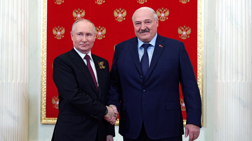 Vladimir Putin and Alexander Lukashenko smile as they shake hands and pose for a photo between two white columns.