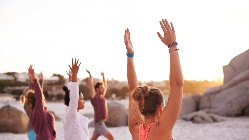 A group of people raise their arms in a yoga pose on the beach