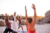 A group of people raise their arms in a yoga pose on the beach