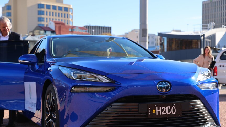 A blue car seen from the front. It's got a Toyota badge and number plate H2GO showing its a hydrogen powered car.