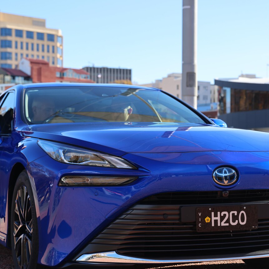 A blue car seen from the front. It's got a Toyota badge and number plate H2GO showing its a hydrogen powered car.
