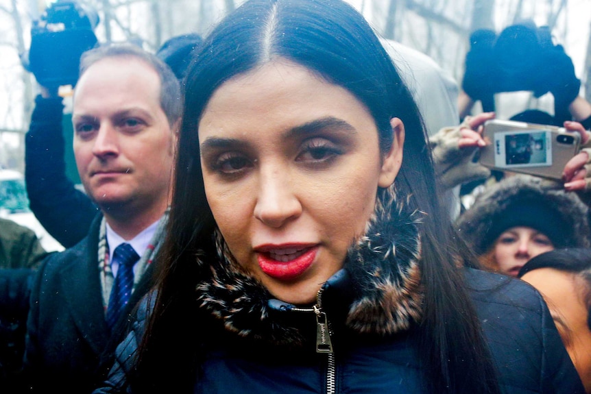 A woman in a fur trimmed coat surrounded by people holding phones and cameras