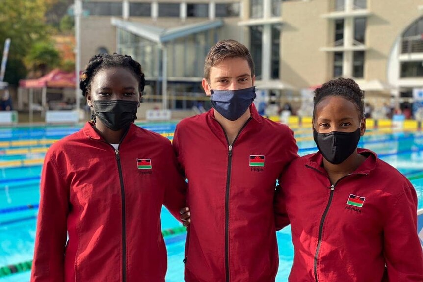 Three people in red tracksuits with face masks on pose for a photo