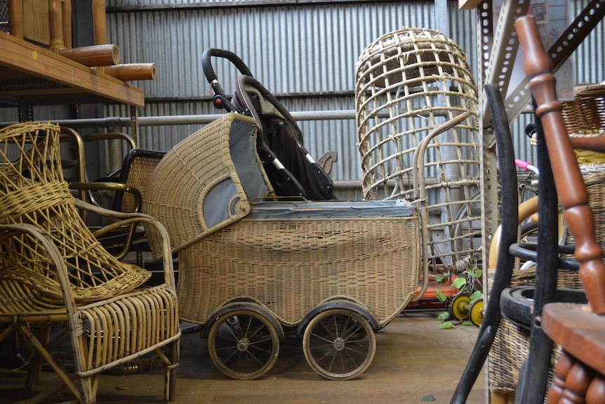 An old pram sits among the props of furniture in a shed.