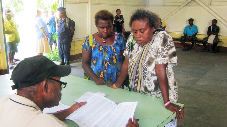 An official checks the names of two Papua New Guinean voters at a polling station in Kokopo