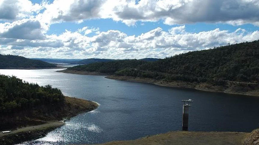 A large dam beneath a bright but cloudy sky, as seen from a high vantage point.