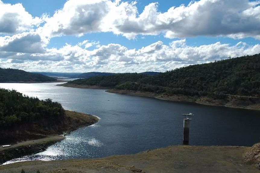 A large dam beneath a bright but cloudy sky, as seen from a high vantage point.
