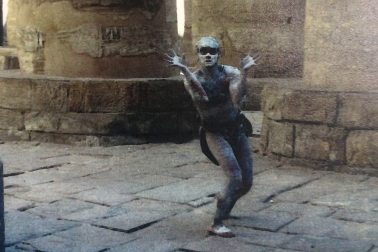 A man in traditional Larrakia body paint dancing near an ancient-looking building with hieroglyphs