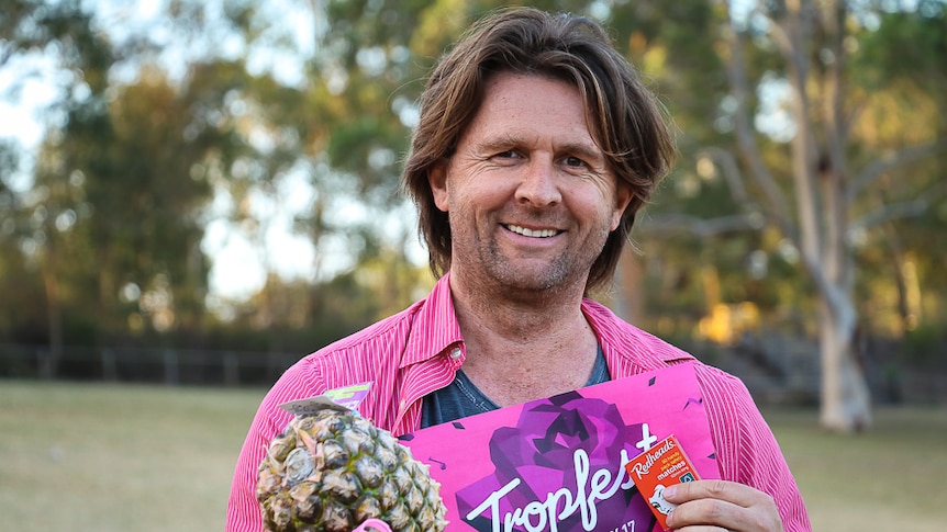 Man wearing a pink t-shirt while holding a pineapple, matches and a slinky.