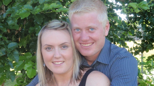 A blonde woman in a black tank top is embraced by a blonde man wearing a blue shirt 