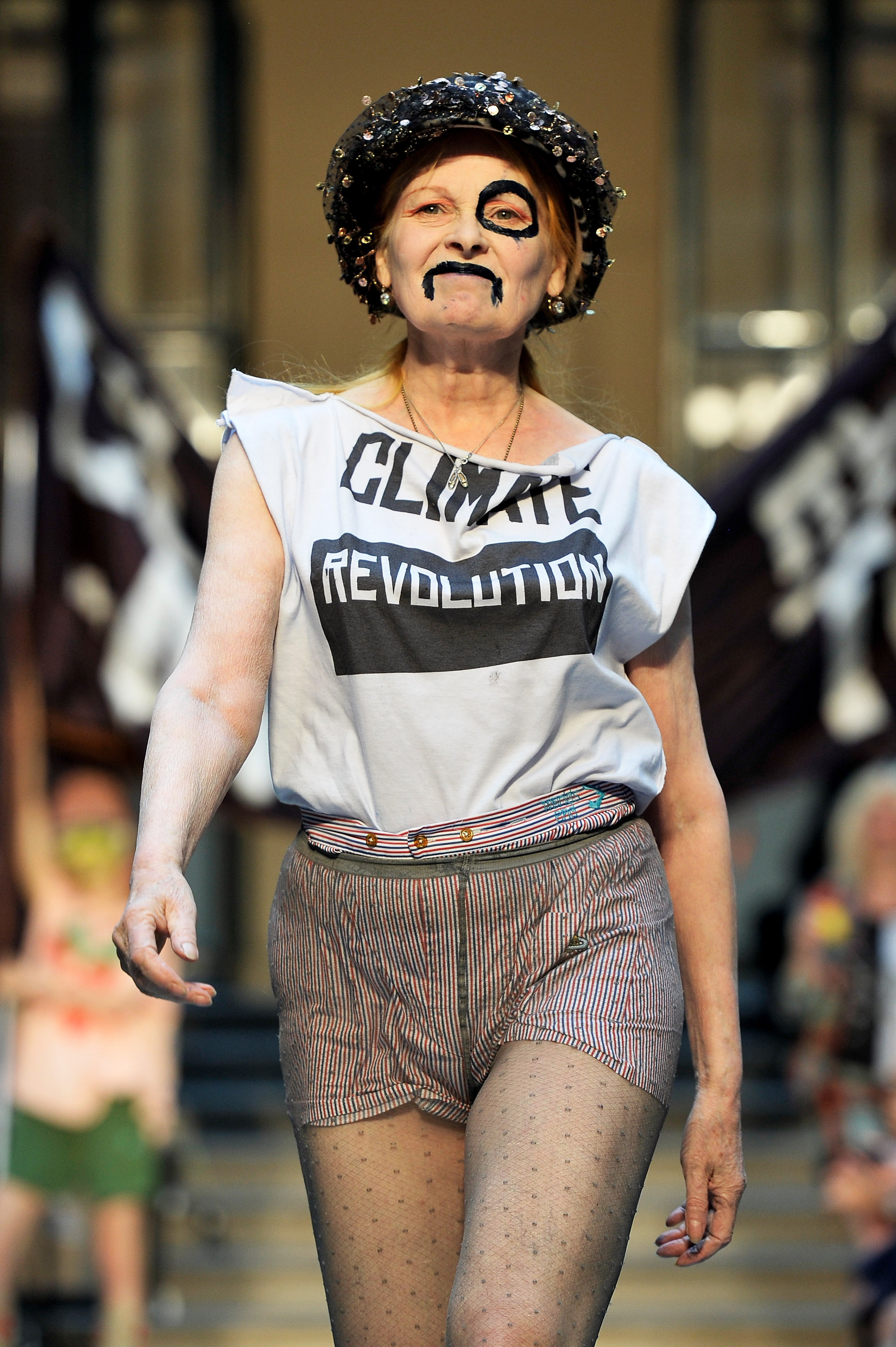 Vivienne Westwood camina por la pasarela con pantalones cortos de tweed y una camiseta que dice 