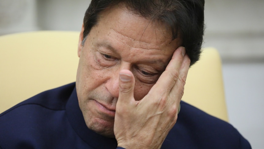 A close-up photo shows Pakistani Prime Minister Imran Khan touching his forehead with his right hand.