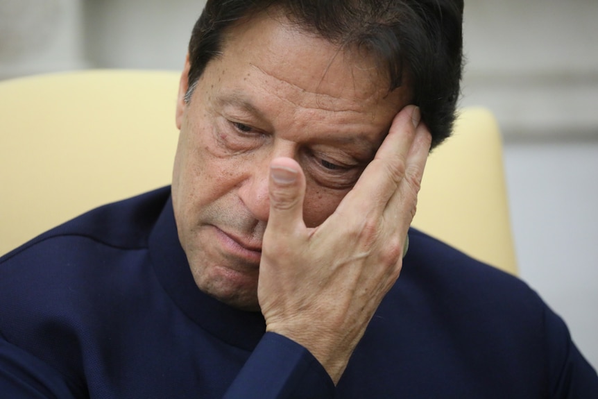 A close-up photo shows Pakistani Prime Minister Imran Khan touching his forehead with his right hand.