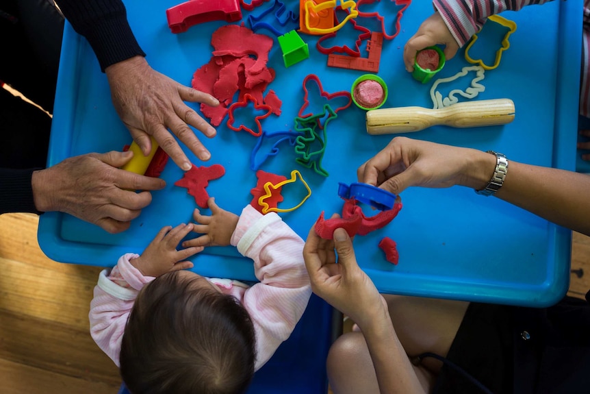 An overhead shot of baby Tia, her mother and another woman playing with playdough and making shapes with biscuit cutters.