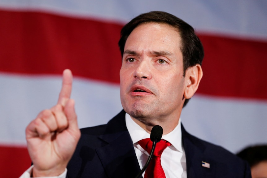 Close up of man speaking while holding one finger up.