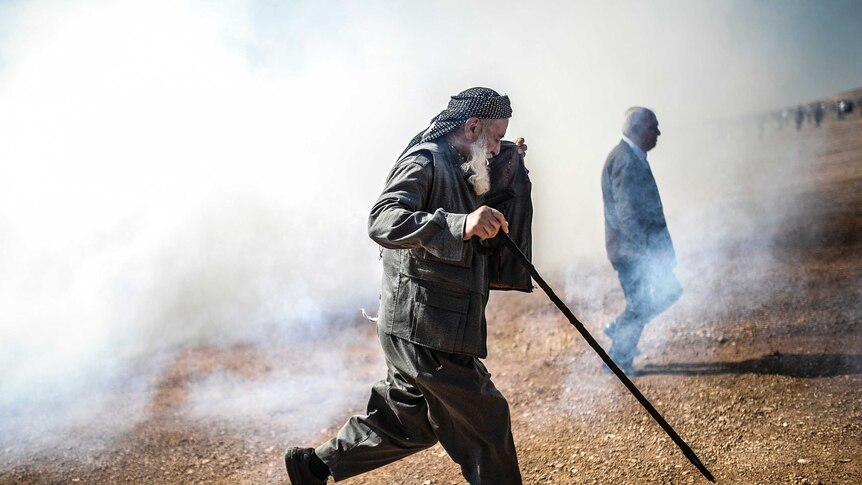 Old Kurdish man runs away from tear gas near Turkish-Syria border crossing