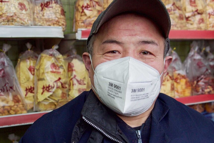 A man wearing a face mask stands in front of snack food in a store