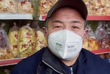 A man wearing a face mask stands in front of snack food in a store