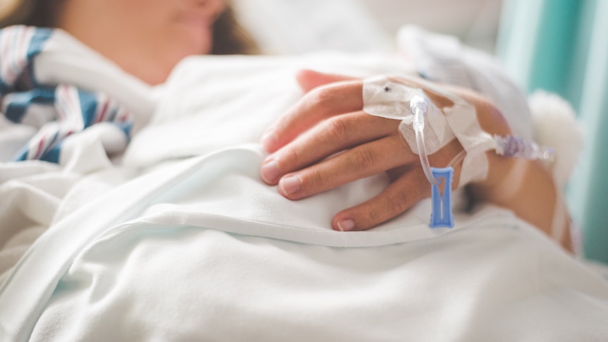 Photo of child in hospital bed with drip on hand in foreground