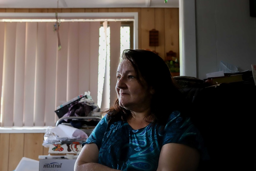 Lisa Baker, sitting on chair inside a loungeroom with shut blinds behind her.