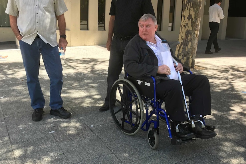 Retired traffic policeman Brian Allen Eddy in a wheelchair outside the Western Australian Coroner's Court in Perth with two men.