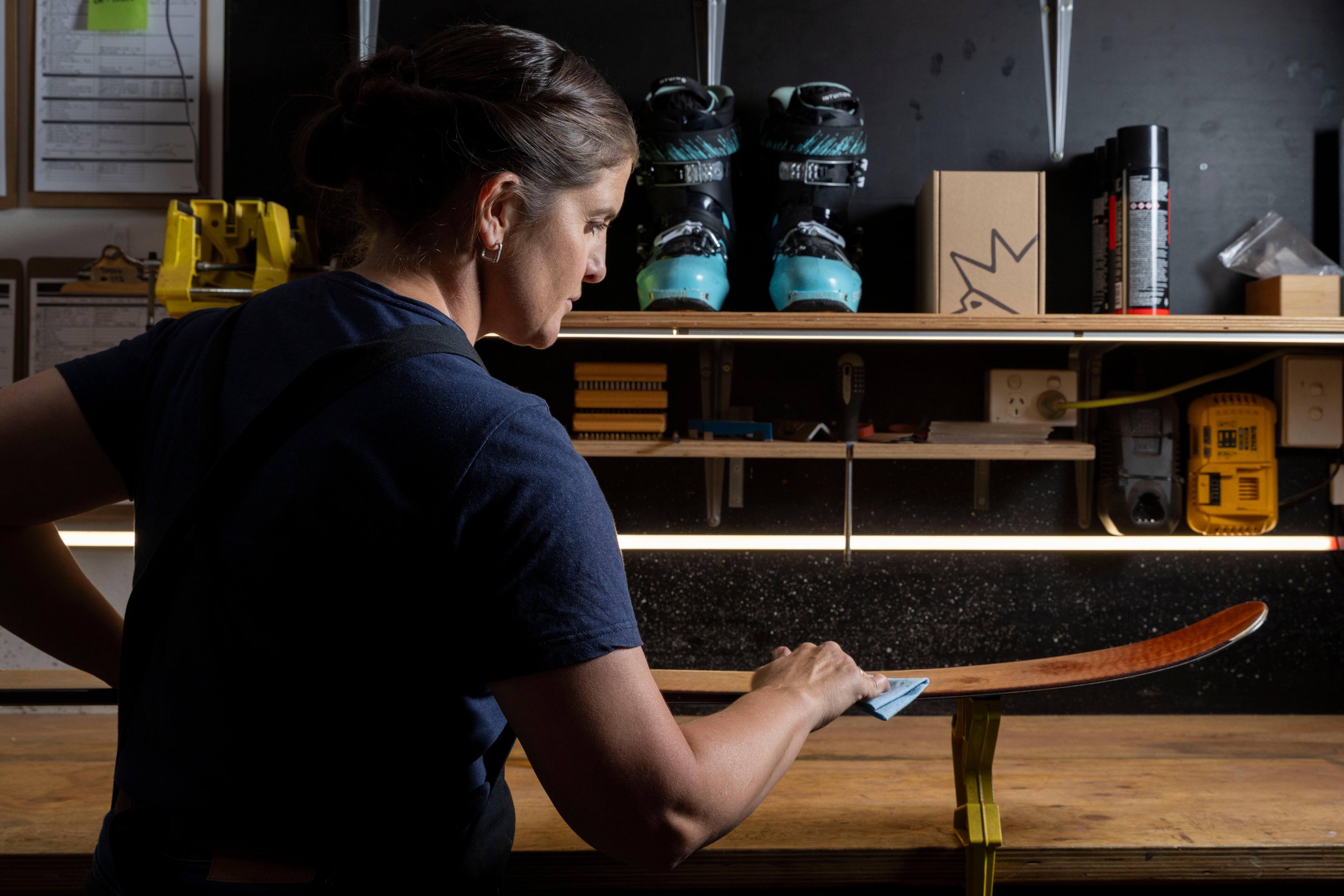 A woman applying oil to skis in a workshop.