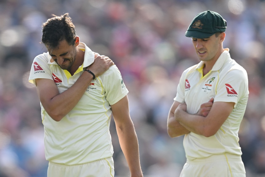 Mitchell Starc grimaces as he holds his shoulder as Pat Cummins looks disappointed next to him
