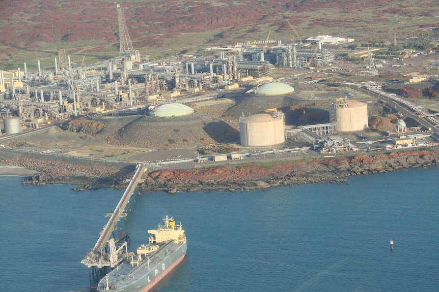 A tanker sits in water while loading with gas from a pipeline