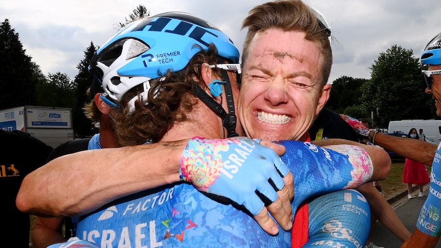 Simon Clarke, with a dirty face after a long ride, smiles from ear to ear while hugging a team mate