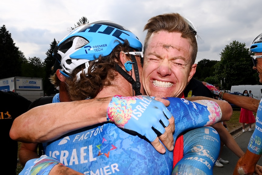 Simon Clarke, with a dirty face after a long ride, smiles from ear to ear while hugging a team mate