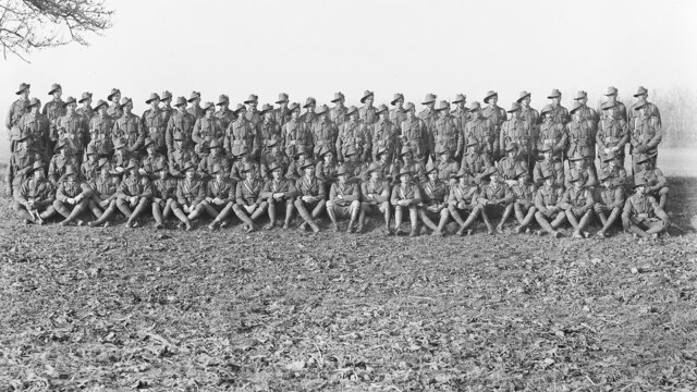 About 80 soldiers pose for a black and white photo in a field.