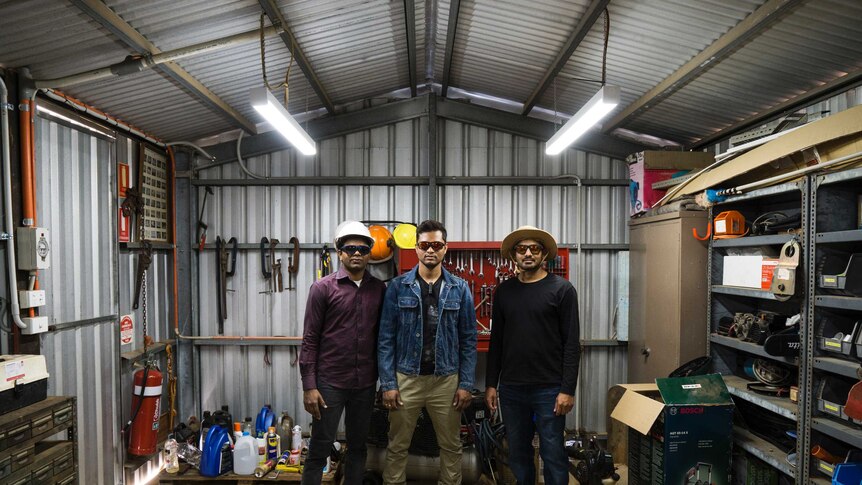Three men standing side by side in a tool shed