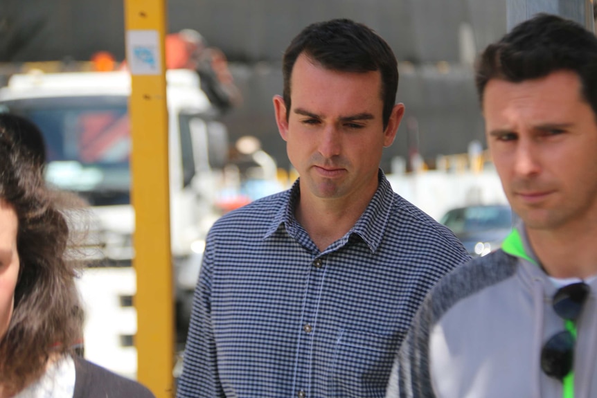 Matthew looks down as he walks, flanked by another man and a woman.