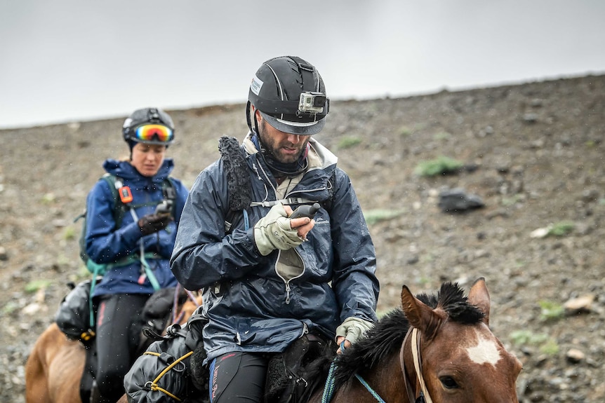 A man and a woman riding on horses looking at GPS devices.