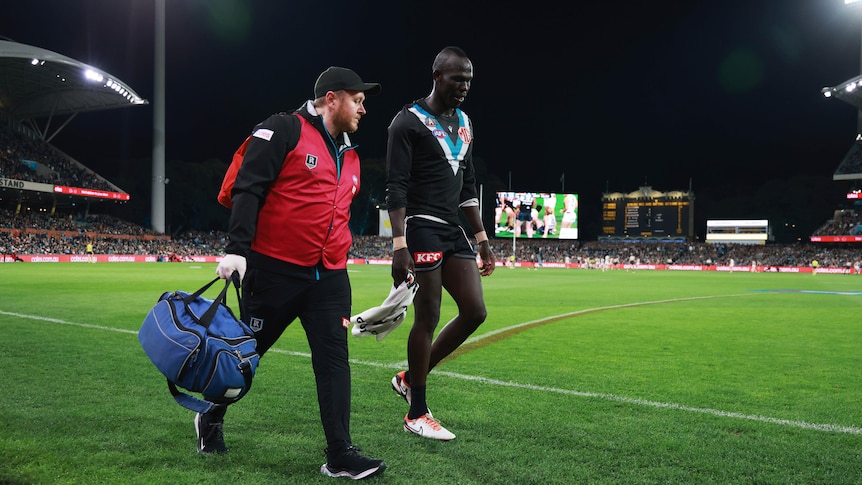 A Port Adelaide defender walks around the boundary with a medical officer after being injured.
