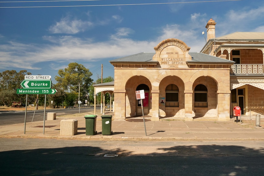  An old sandstone building next to a street sign pointing to Bourke one way, Menindee the other.
