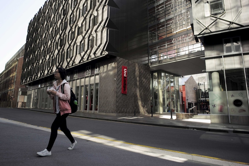 A young woman walks away from a large multi-storied univeristy accommodation building.