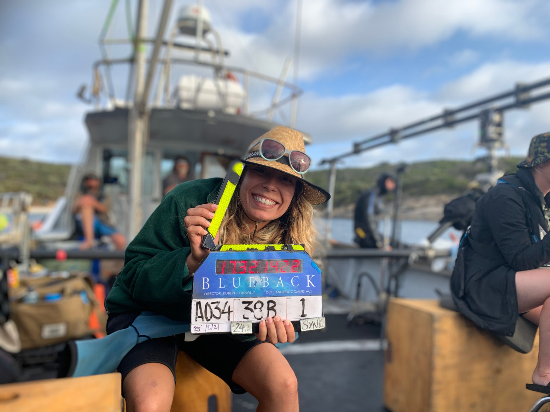 A woman with a clapper board on a boat on a film set.
