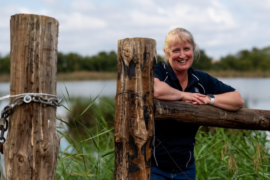 A woman smiles while leaning onto a wooden fence.