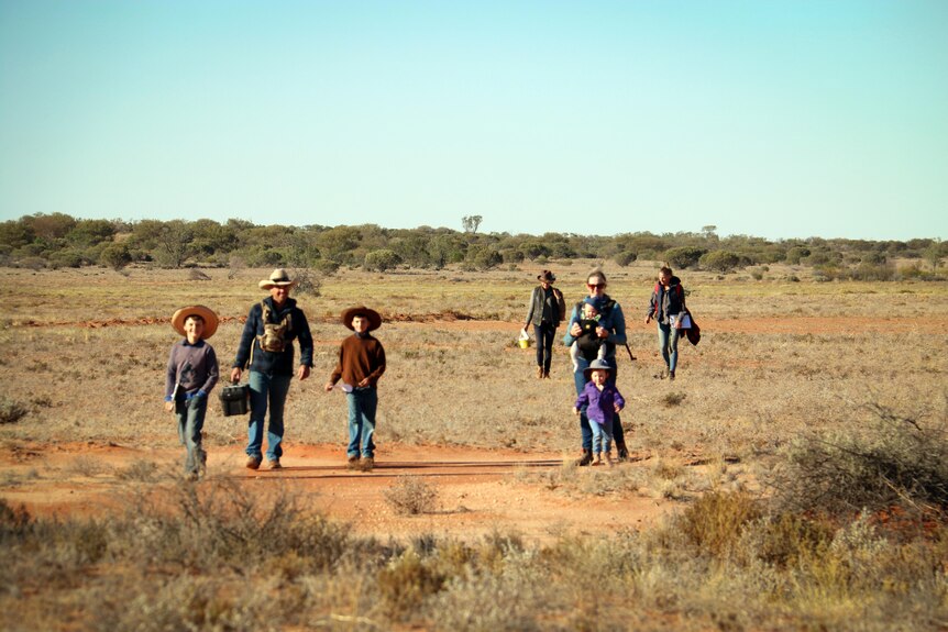 Four adults and four children in sparse outback walking as a scattered group