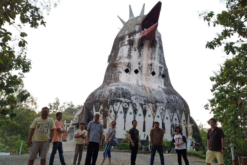 Nine people pose in front of house shaped like a chicken.