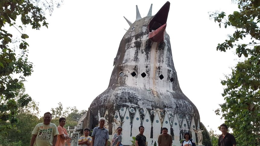 Nine people pose in front of house shaped like a chicken.