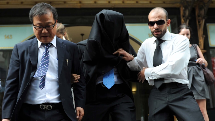 Song Chhoung Ea (centre), the owner of a Sydney brothel, hides his face as he leaves the Downing Centre Court