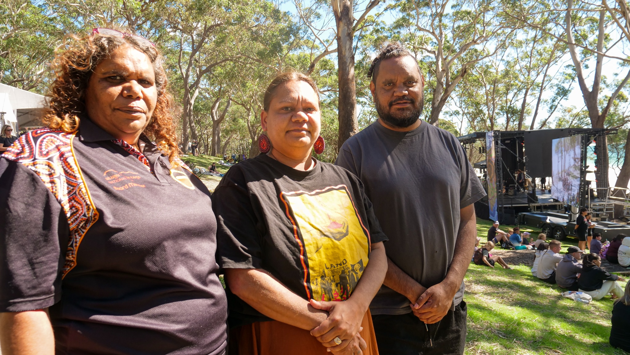 Мужчина и две женщины из числа коренных народов улыбаются, носят коричневые рубашки с логотипами, дизайн коренных народов.