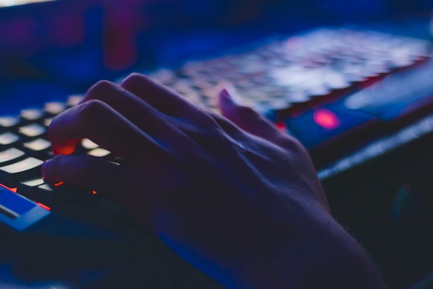 Close up of a hand typing on a keyboard in a dark room